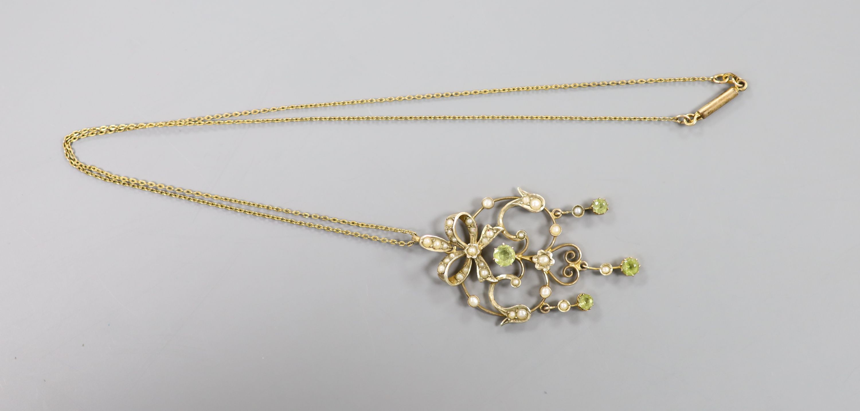 An Art Nouveau 9ct, peridot and seed pearl set scroll pendant, 46mm, gross 3.4 grams, on a gilt metal chain.